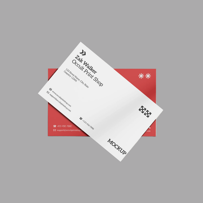 A white business card mockup layered diagonally over a red rectangular card, shown on a plain gray background. The front card includes black text, logos, and contact details, with the word MOCKUP printed near the bottom.