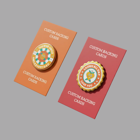 Two circular enamel pins displayed on custom backing cards against a solid gray background. The left pin is on an orange card and reads 'FLOWER GIFT EVERY DAY'; the right pin is on a red card and reads 'LAUGH ALL DAY LOVE YOU'.