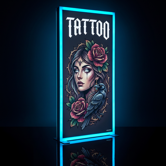 A vertical illuminated sign displaying a tattoo-style illustration with the word "TATTOO" at the top, featuring a woman's face, roses, leaves, and a raven. The sign has a glowing blue border and is shown against a dark background with a reflection below.