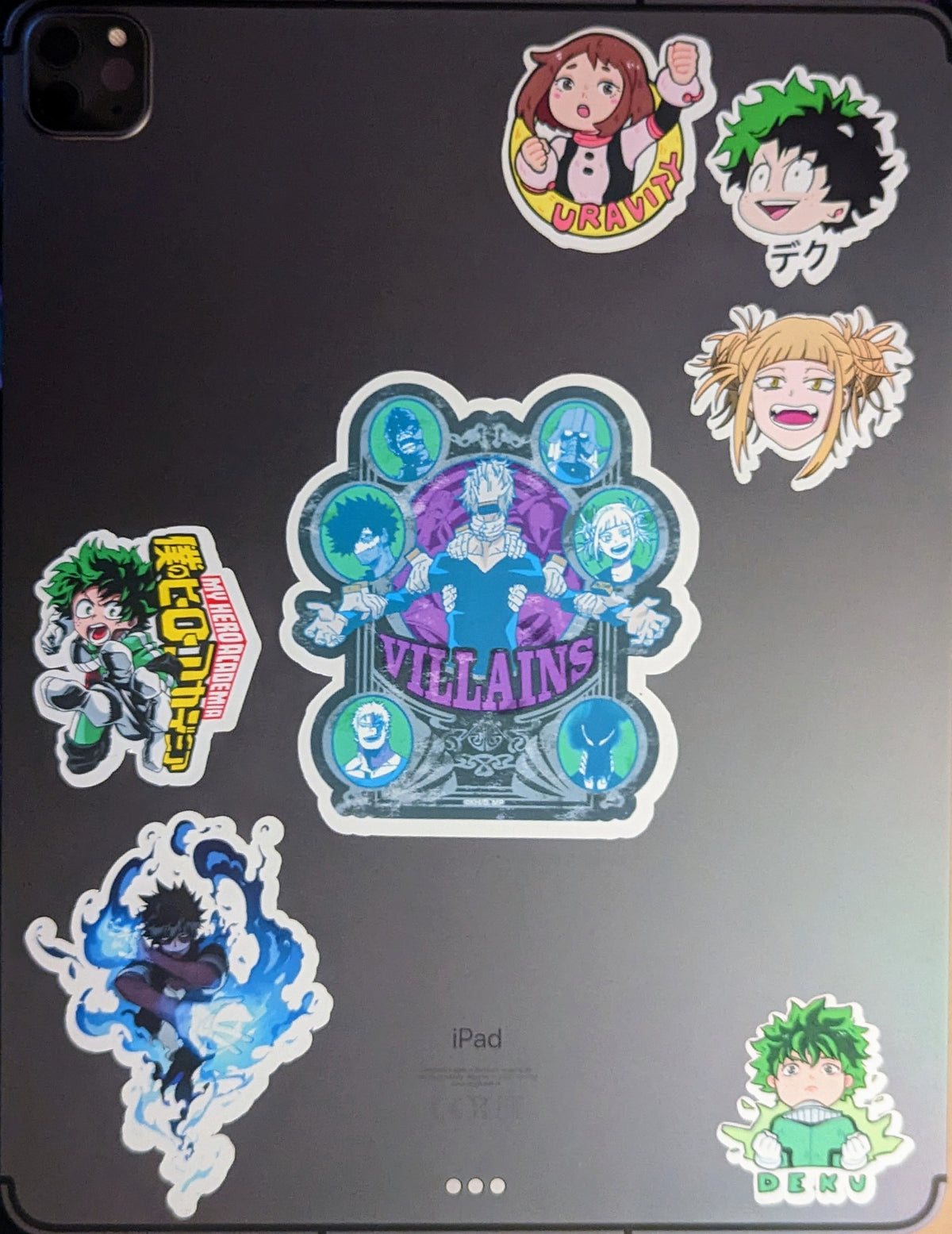 A dark gray iPad decorated with multiple colorful anime stickers from My Hero Academia, featuring characters like Deku, Uravity, and others, with the word 'VILLAINS' in the center.