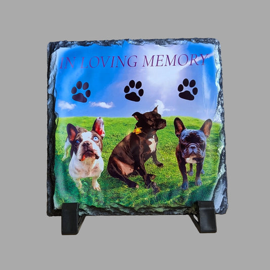 Memorial plaque with three dogs on a grassy field and 'In Loving Memory' text.